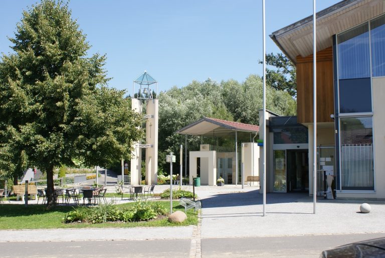 Modern gestalteter Dorfplatz in Lebing mit Kirche, Sitzgelegenheiten, Begrünung, Bankomat.