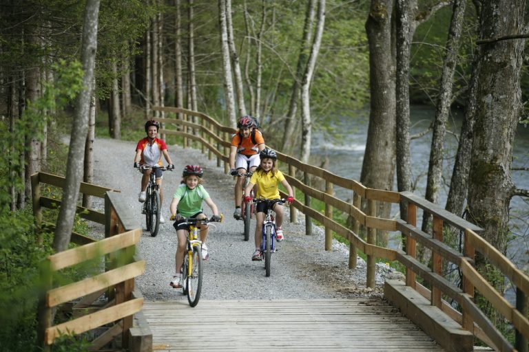 Eine Familie fährt über den breit ausgebauten Feistritztalradweg durch den Wald
