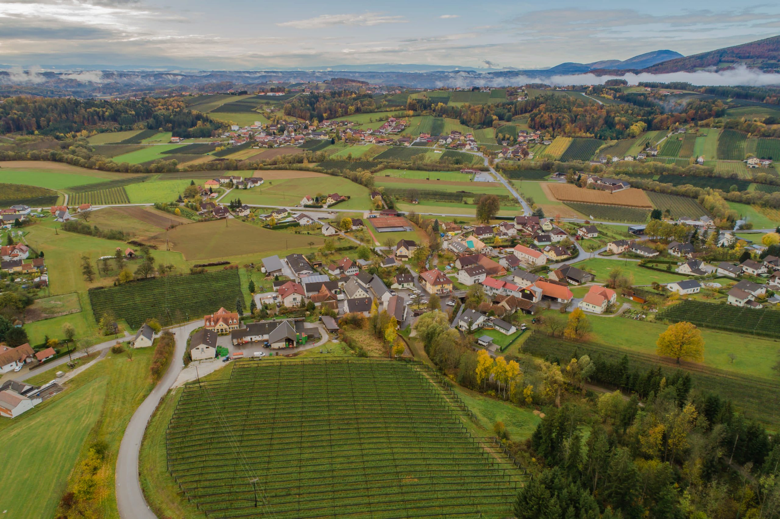 Luftaufnahme von Floing. Kompakter Ortskern umgeben von Obsthängen und Ackerflächen sowie kleinen Wäldern