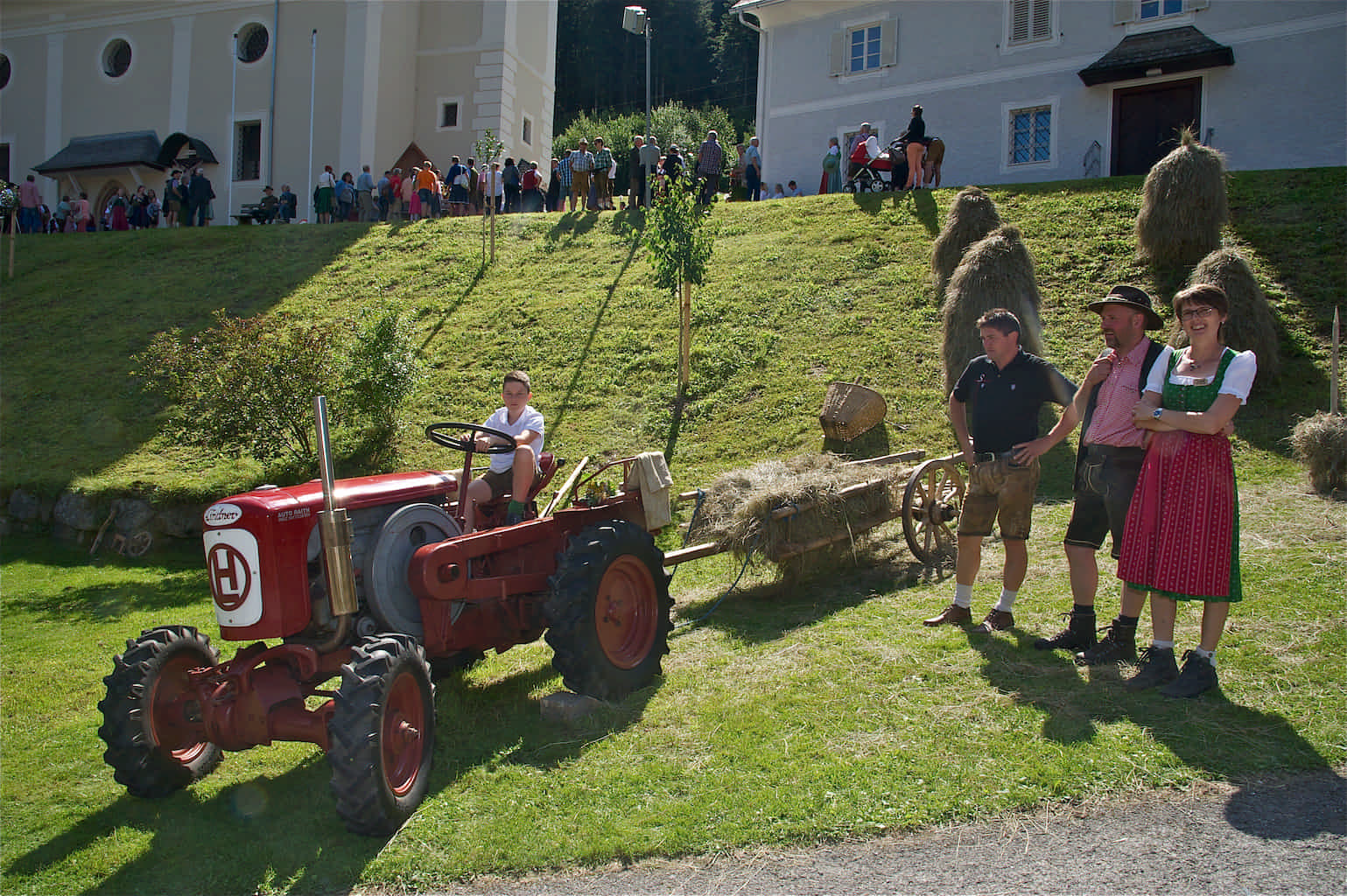 Ein junge sitzt auf einem kleinen roten Oldtimer Traktor vor der Gasener Pfarrkirche