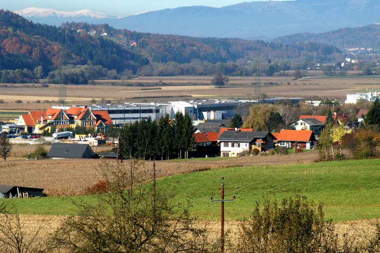Blick vom Hoschkaberg auf den Ortsteil Hofstätten-Obertrum. Während leicht erhöht Einfamilienhäuser stehen, befindet sich ganz am Talgrund ein großer Betrieb