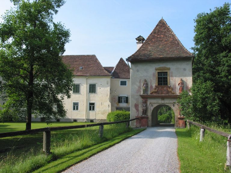 Durch das Tor des Schlosses Stadl führt eine Schotterstraße, die links und rechts durch einen einfachen Holzzaun begrenzt