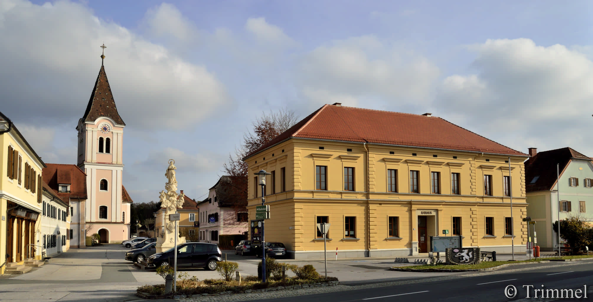 zweigeschossiges historisches Rathaus Neudau mit gelber Fassade. Im Hintergrund befindet sich die Kirche
