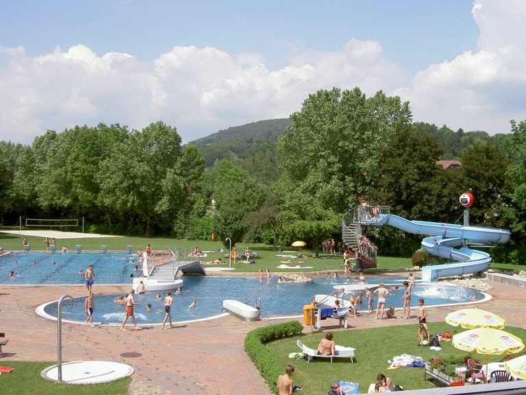 Erlebnisbad in Pöllau mit Schwimmbecken und Wasserrutsche und Volleyballplatz. Das große Becken ist geteilt in einen Sportbeckenteil sowie einen Nichtschwimmerbereich.