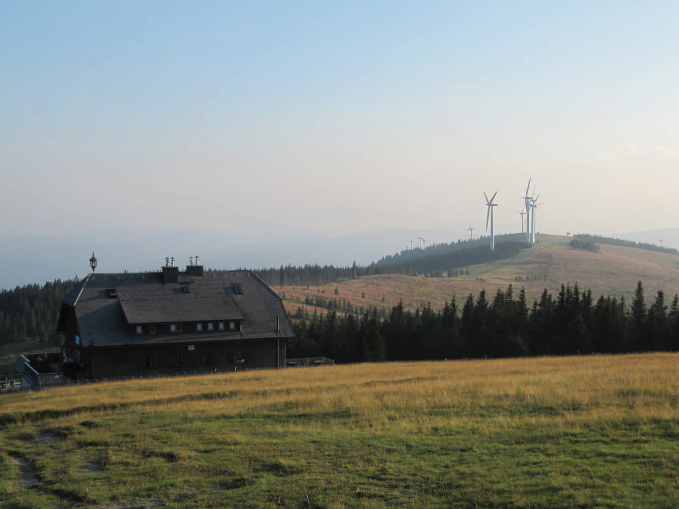Auf einem Bergrücken steht eine Schutzhütte sowie im Hintergrund etliche Windkraftwerke