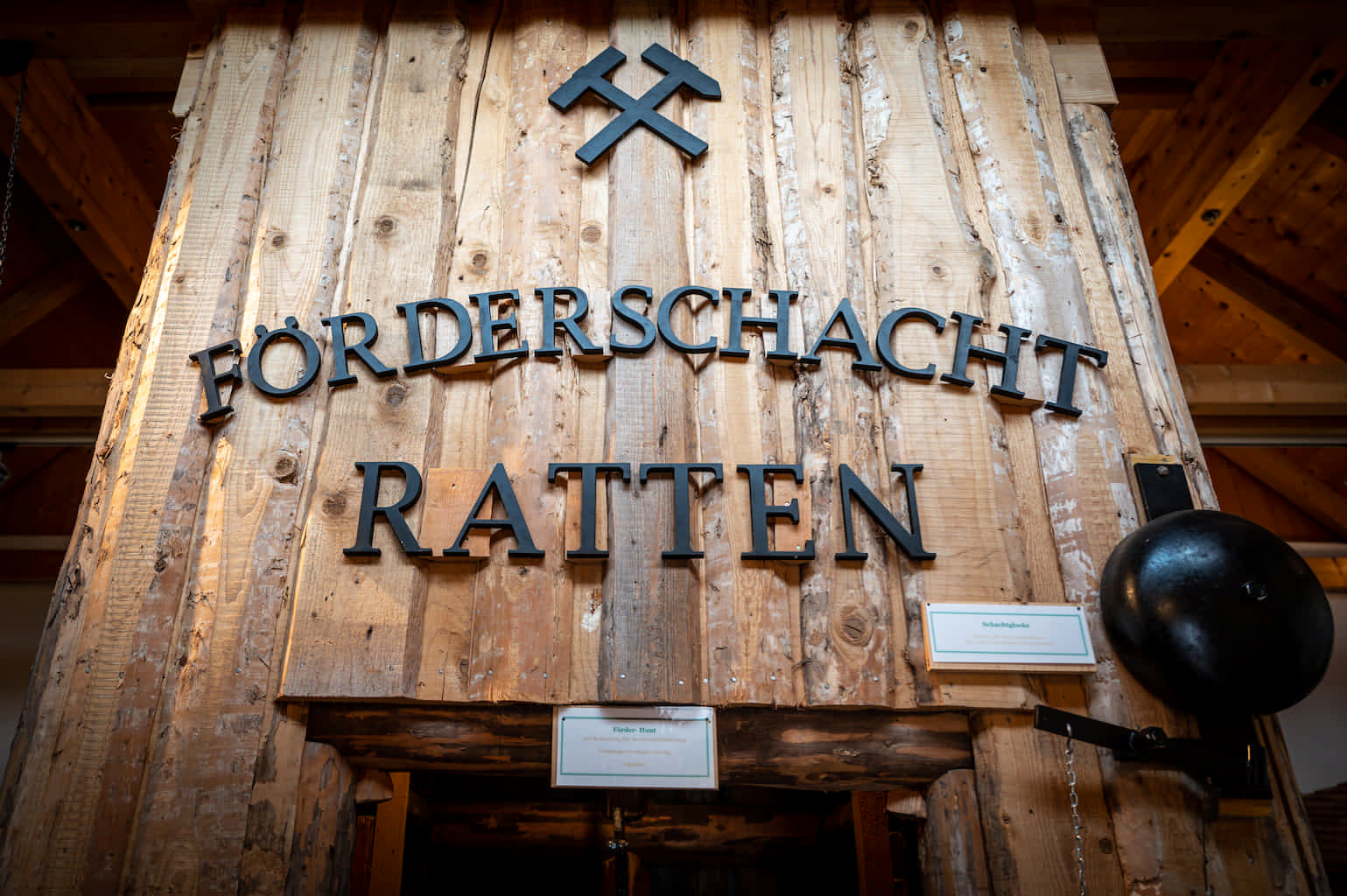 Förderschacht-Nachbildung aus Holz in einem Museum. Über dem Eingang sind zwei gekreuzte Hämmer sowie der Schriftzug "Förderschacht Ratten" angebracht