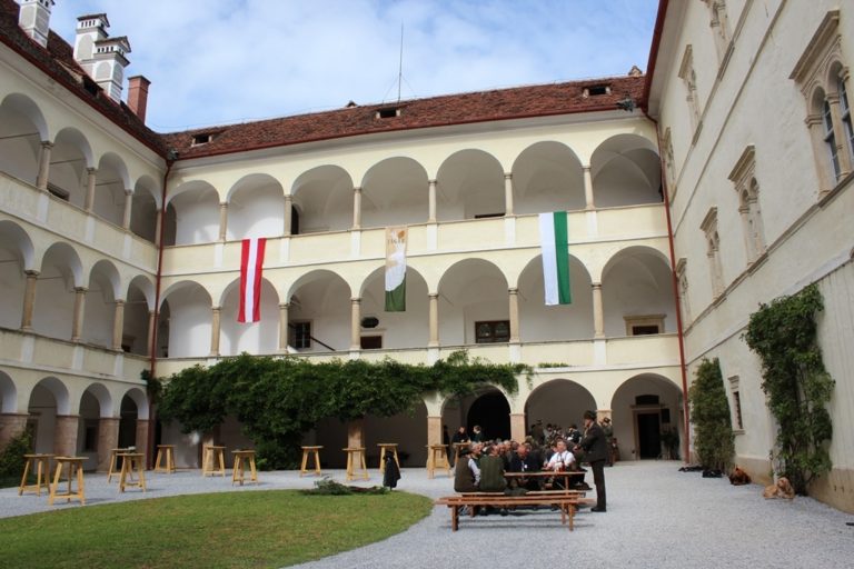 Innenhof des Schlosses Thannhausen mit Stehtischen, Wiese und Sitzgelegenheiten. Das Schloss weist innen offene Arkadengänge auf